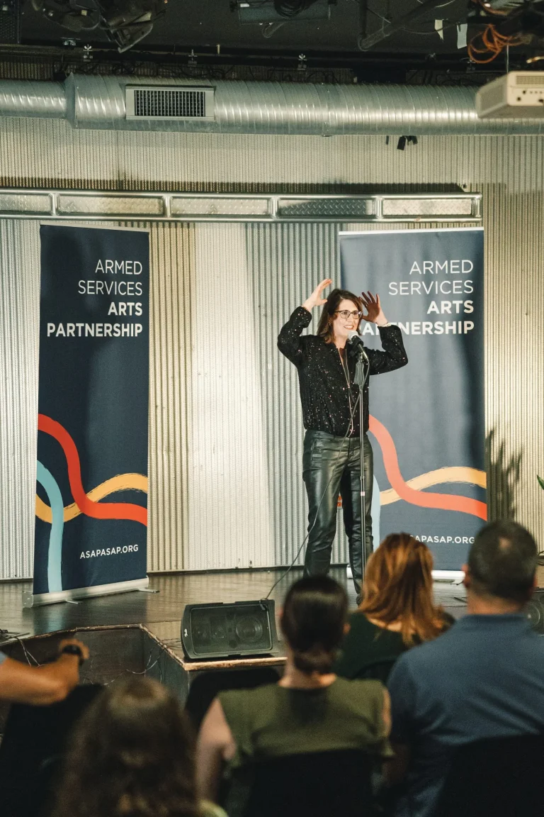 Lauren Lobrano performing on stage during the Armed Services Arts Partnership Storytelling Bootcamp graduation showcase before a live audience.